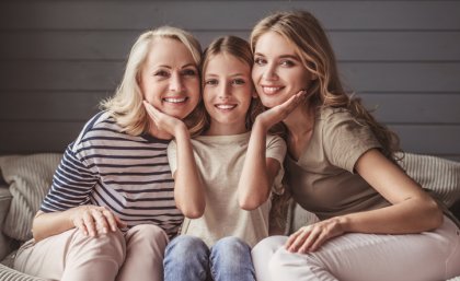 Three generations of women sit on a couch.